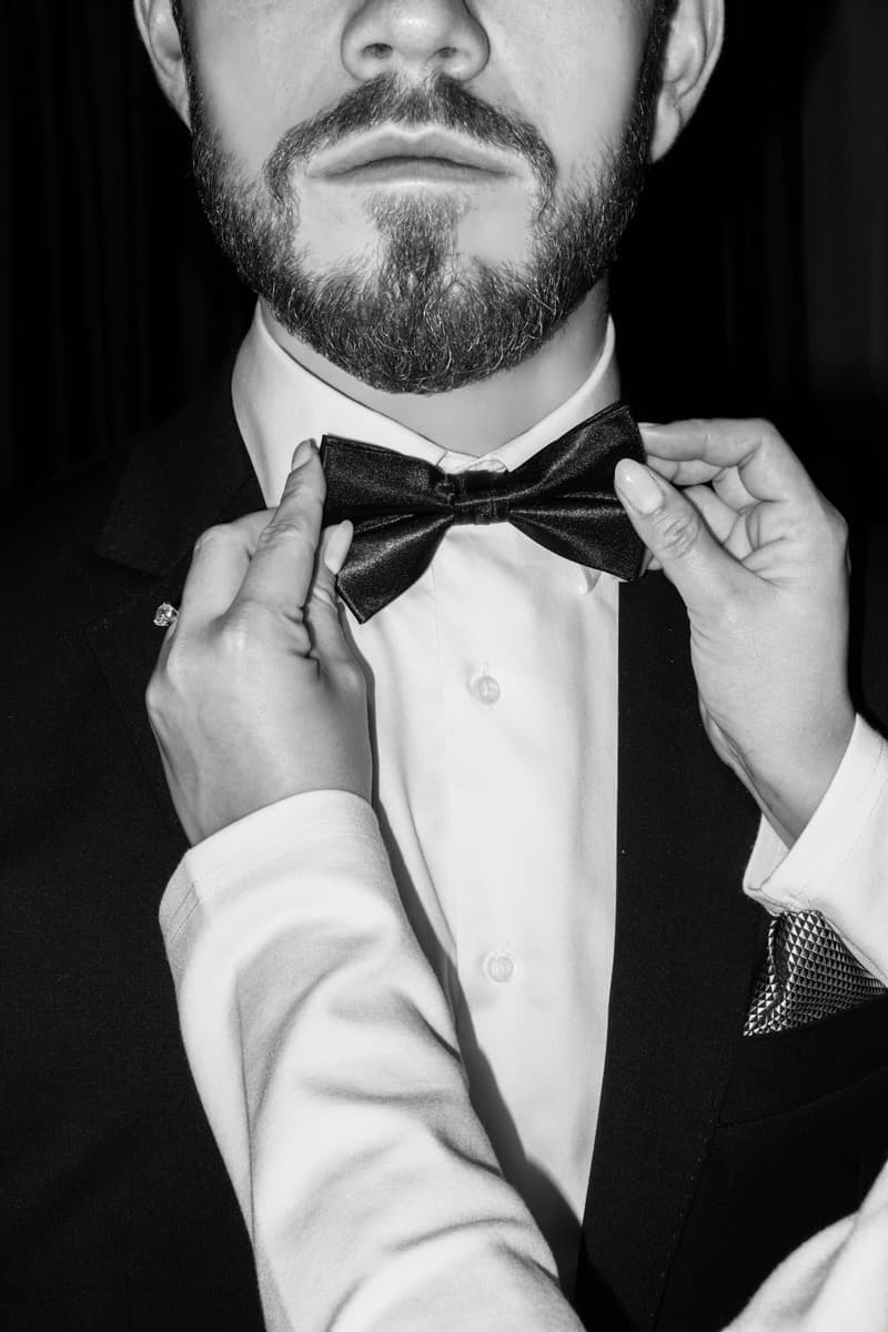 Hombre ajustándose la corbata de moño negra de un esmoquin, en blanco y negro